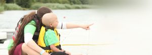 a child with cancer having water sports with a volunteer overlooking a pond